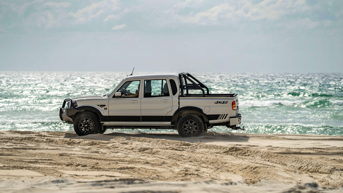 Scenic shot of a Mahindra pick-up truck by the shoreline of a sandy beach.