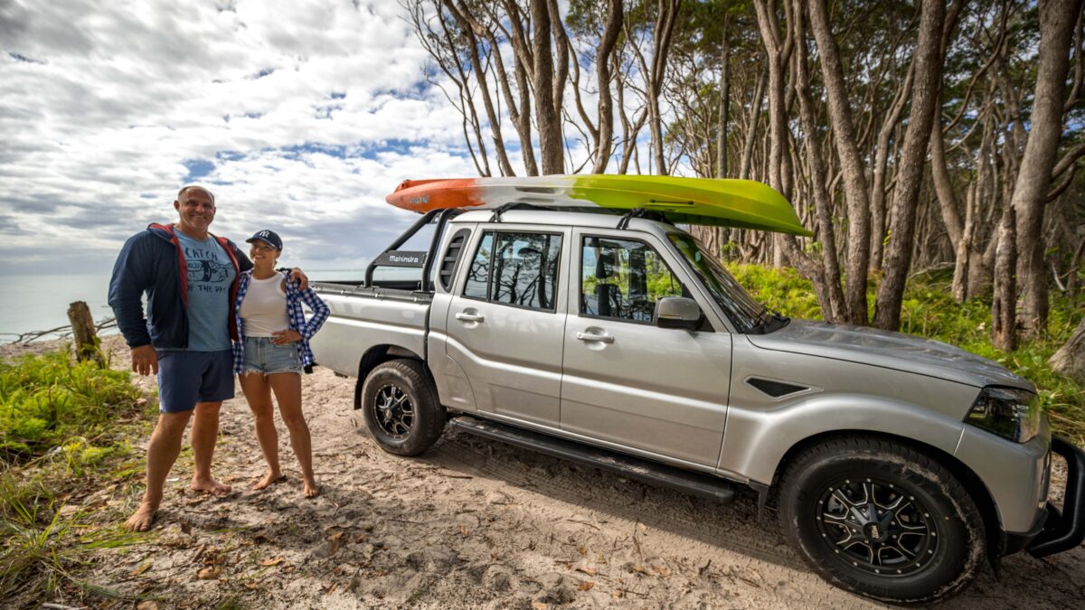 A smiling couple preparing for a kayaking trip, their Mahindra pick-up truck prominently featuring a kayak on its roof.